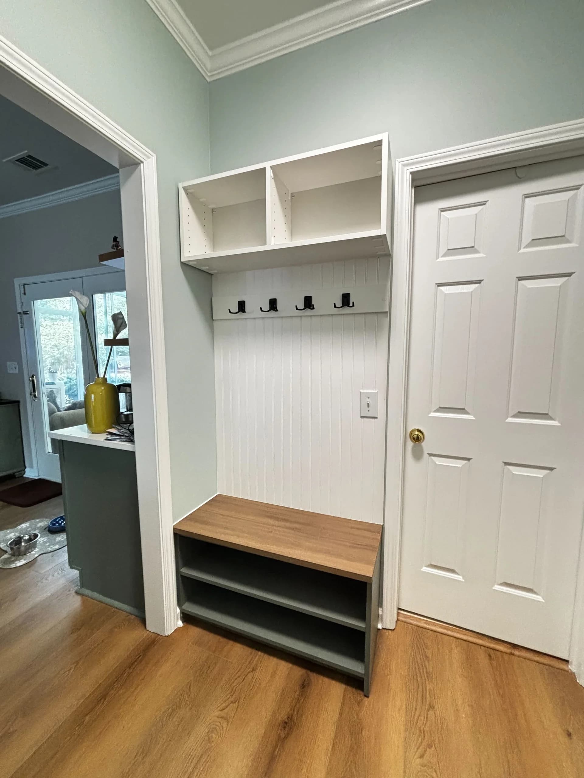 White mudroom nook with wood bench, shoe shelf, and coat hooks